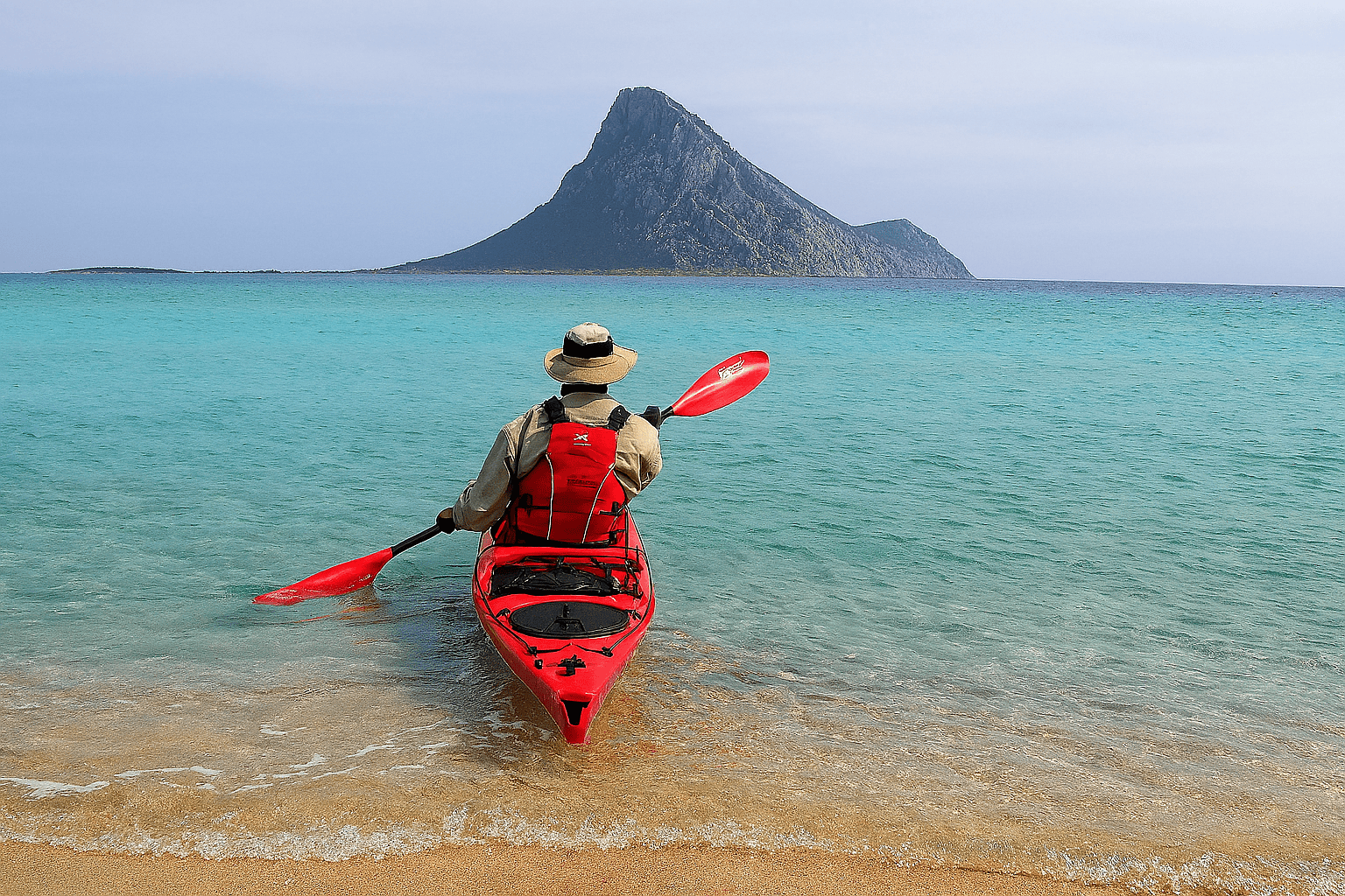 Person kayaking towards a mountain on a calm turquoise sea.