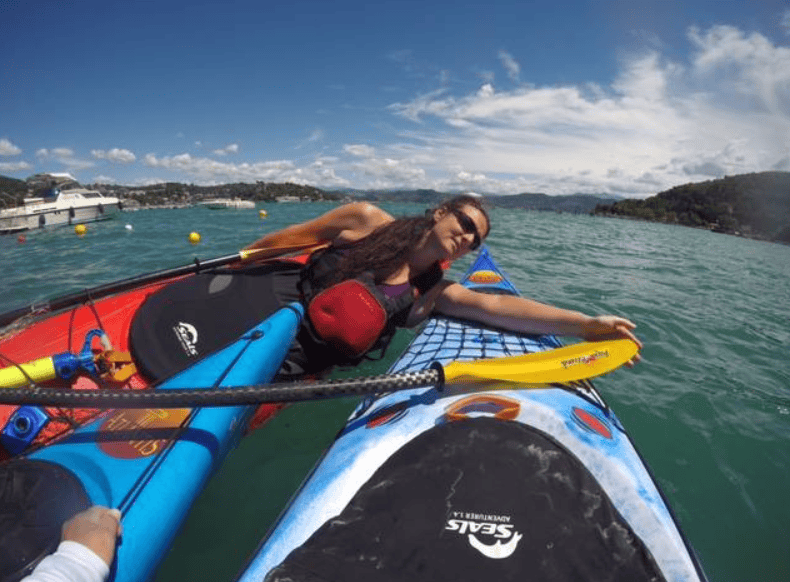 A woman lying on a kayak in calm water, in the waters of Italy, surrounded by other kayaks on a sunny day.