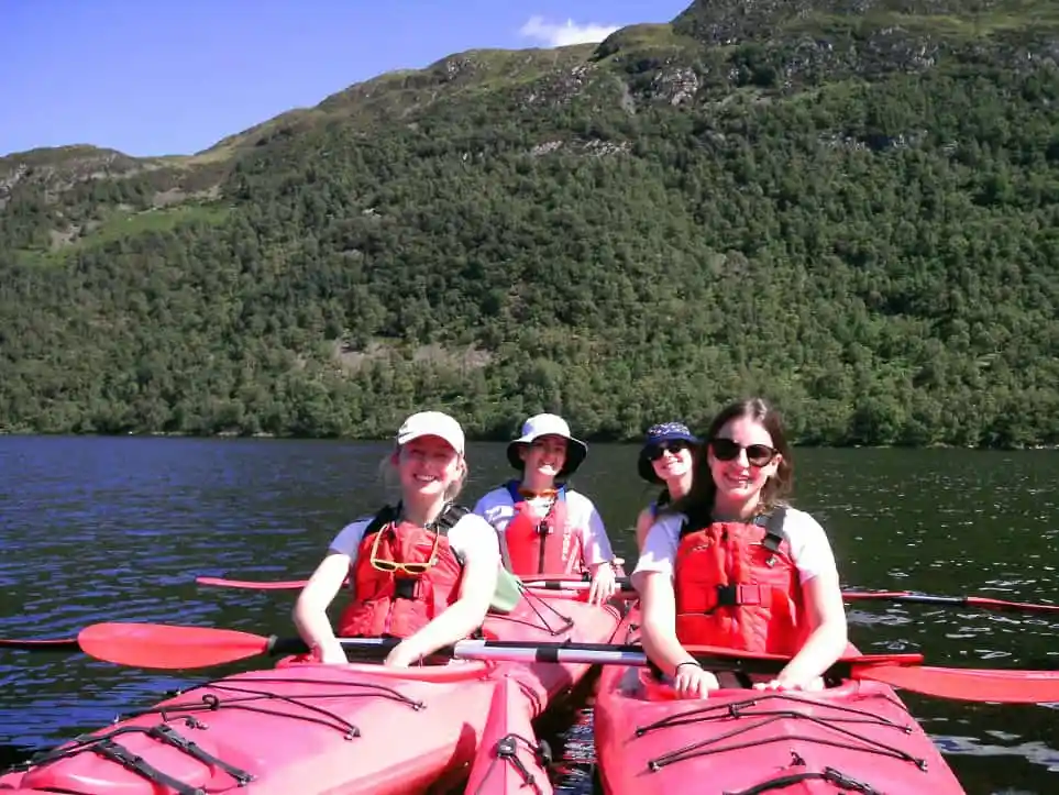 Enjoy a scenic kayaking experience Four people kayaking on a lake with green hills and clear sky in the background.