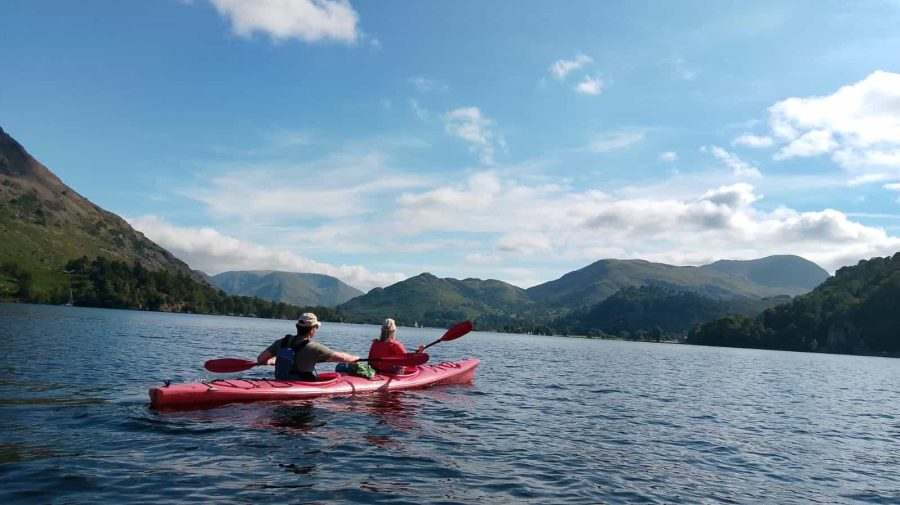 Two people kayaking on a lake surrounded by mountains under a beautiful sky.