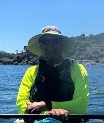 Person kayaking on a sunny day, wearing a sun hat and sunglasses.