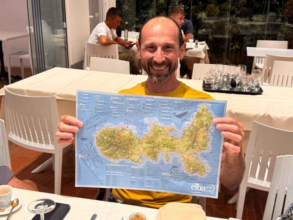 Man smiling, holding a map while seated at a restaurant table.