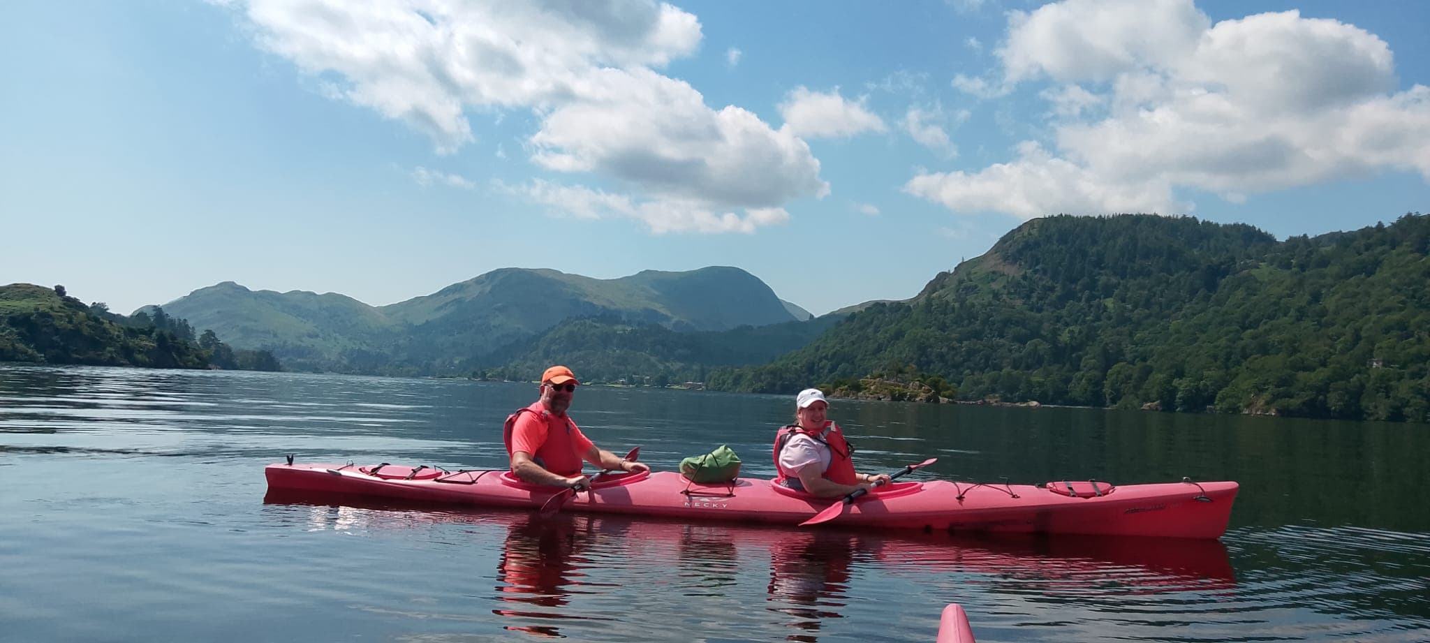 Two people kayaking on a calm lake with mountains in the background.