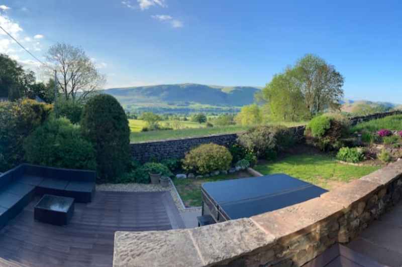 Scenic view of a garden with hills and trees under a clear blue sky.